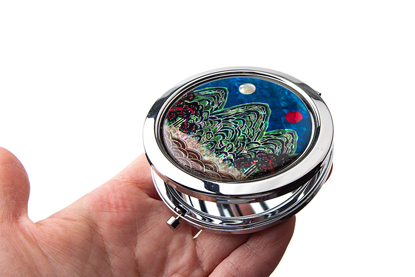 원형 금속 테두리 위에 자개 상감 기법으로 표현된 일월오봉도 산수문, 청록과 청색의 대비와 붉은 해·흰 달이 돋보이는 손거울 디자인