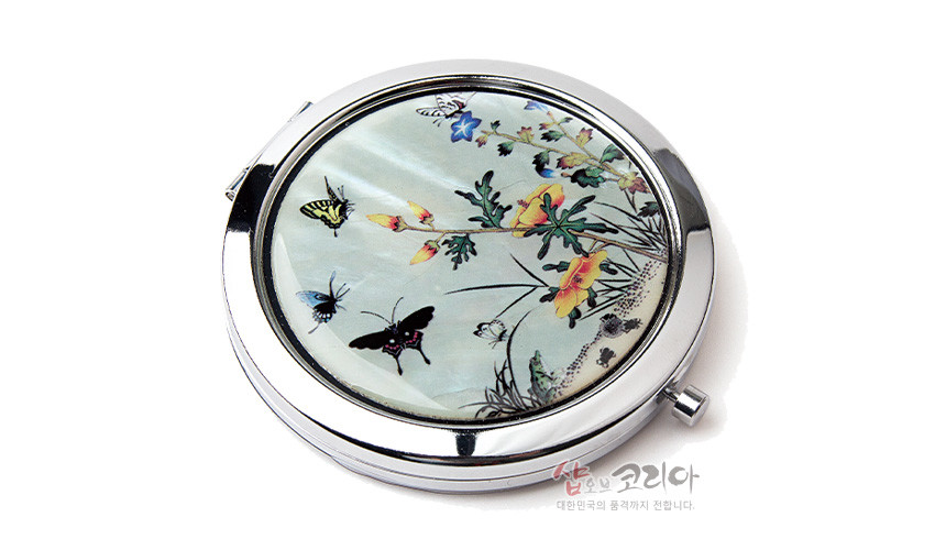 [텍스트: 샵오브코리아 대한민국의 품격까지 전합니다.] 진주빛 천연 자개 바탕에 상감 기법으로 꽃과 나비, 풀벌레 초충도 문양을 섬세하게 표현한 원형 금속 손거울 디자인