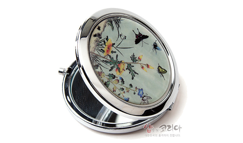 [텍스트: 샵오브코리아 대한민국의 품격까지 전합니다.] 금속 테두리에 초충도 문양을 담은 타원형 자개 손거울, 나비와 꽃, 풀벌레를 섬세하게 표현한 은은한 색감의 자개 장식