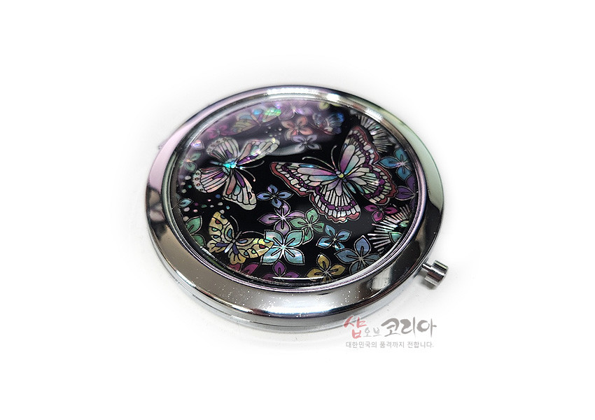 [텍스트: 샵오브코리아 대한민국의 품격까지 전합니다.] 검은 옻칠 바탕 위에 오색 자개 상감으로 꽃과 나비 문양을 정교하게 새긴 금속 테두리 원형 손거울 디자인