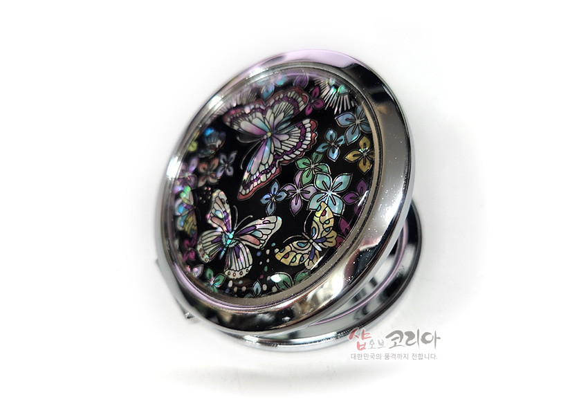 [텍스트: 샵오브코리아 대한민국의 품격까지 전합니다.] 검은 바탕 위에 오색 자개 상감 기법으로 섬세한 나비와 꽃 문양을 넣은 은색 금속 테두리 원형 손거울 디자인
