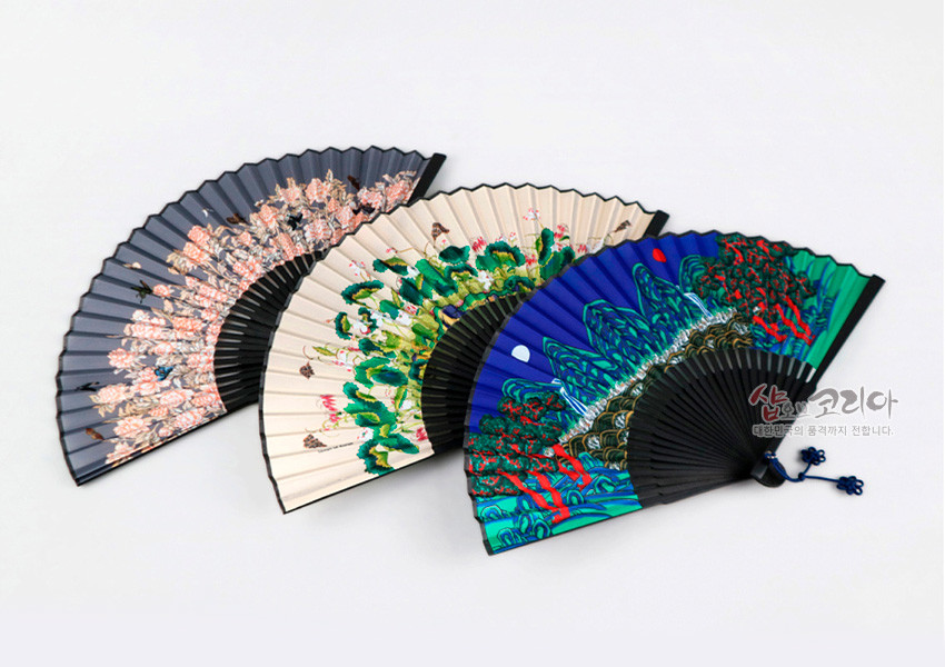 [텍스트: 샵오브코리아 대한민국의 혼을 세계까지 전합니다.] 종이 재질 접이식 부채, 검은색 살과 매듭 장식, 분홍 매화·연녹색 연꽃·청록 산수 등 다채로운 민화 문양 구성