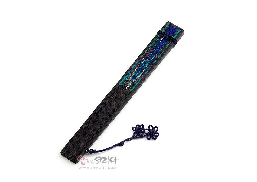 [텍스트: 샵오브코리아 대한민국의 품격까지 전합니다.] 짙은 흑색 대에 남색과 청록색이 어우러진 일월오봉도 민화 채색 장식, 남색 매듭과 고리가 더해진 접이식 전통 부채 모습