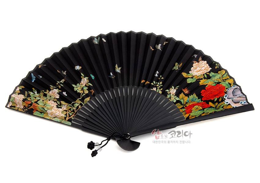 [텍스트: 샵오브코리아 대한민국의 품격까지 전합니다] 검은 꽃무늬 비단 재질 접이식 부채, 붉은·흰 모란과 나비 민화 문양 채색, 하단 매듭 장식 포인트 디자인