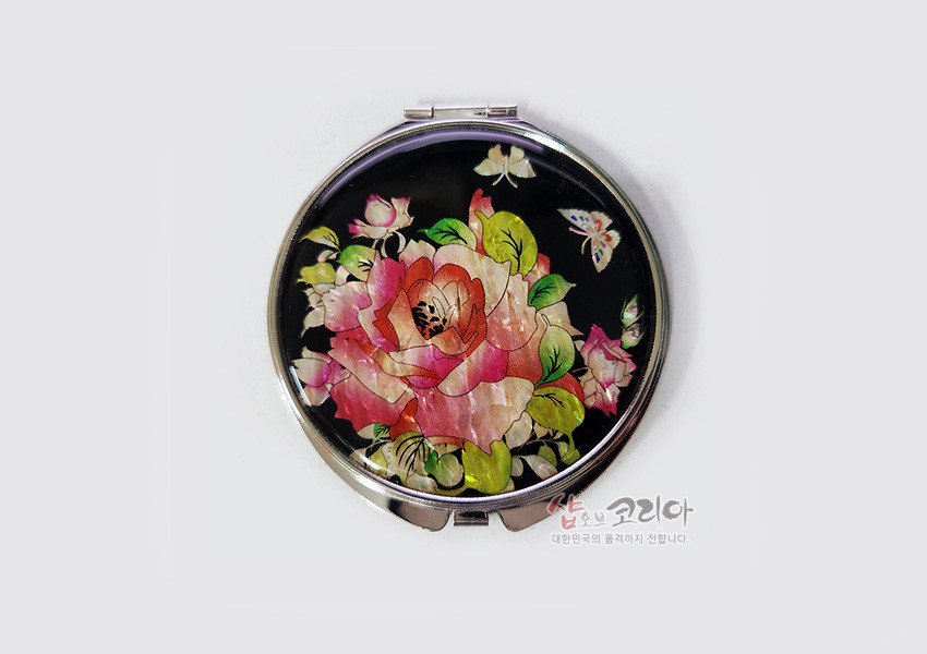 [텍스트: 샵오브코리아 대한민국의 품격까지 전합니다] 검은 바탕 위 자개 상감 기법으로 표현된 장미와 나비 문양이 돋보이는 원형 금속 손거울 디자인