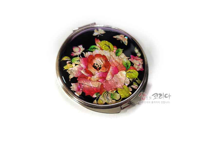 [텍스트: 샵오브코리아 대한민국의 품격까지 전합니다.] 검은 바탕 위 천연 자개 상감 기법으로 표현된 장미꽃과 나비 문양, 은은한 금속 테두리의 원형 손거울 디자인