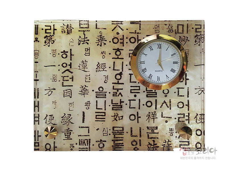 [텍스트: QUARTZ] 한지 질감 바탕 위에 훈민정음 서체 문양을 인쇄하고 금속 테두리 원형 시계와 황금색 장식 나사를 배치한 직사각 탁상시계 디자인