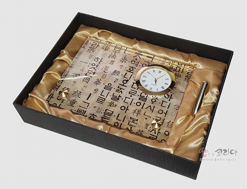 [텍스트: 샵오브코리아 대한민국의 품격까지 전합니다] 한지 위 훈민정음 서체 인쇄와 금속 테두리 원형 시계, 황금색 광택 천과 금속 펜이 조합된 세트형 탁상시계 구성