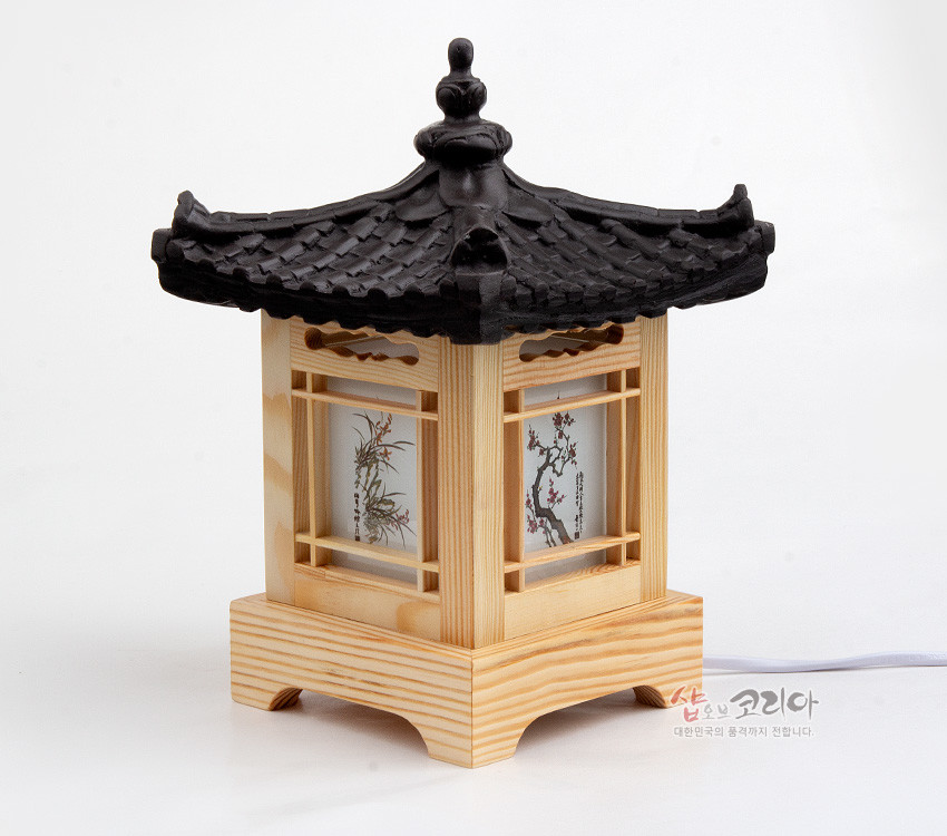[텍스트: 샵오브코리아 대한민국의 품격까지 전합니다.] 나무 기단과 창살 구조 위 검은 기와 지붕을 얹은 사각 좌등, 반투명 창에 사군자 채색화 문양이 들어간 조명 장식