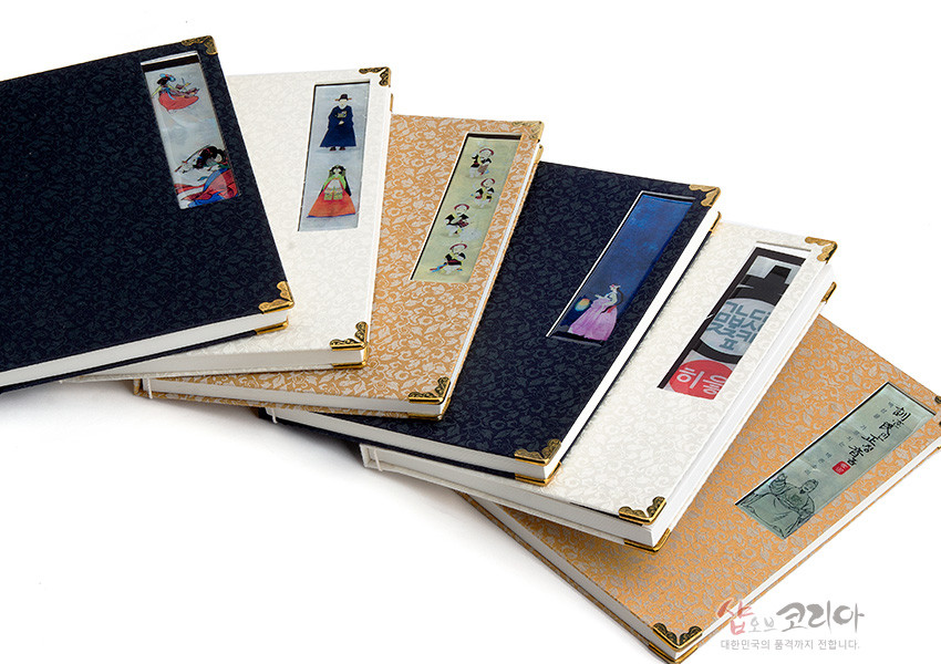 [텍스트: 히읗, 샵오브코리아, 대한민국의 품격까지 전합니다.] 아이보리·남색·금색 비단 표지에 금속 모서리 장식과 자개풍 삽화 패널을 더한 전통 오침노트 구성 모습