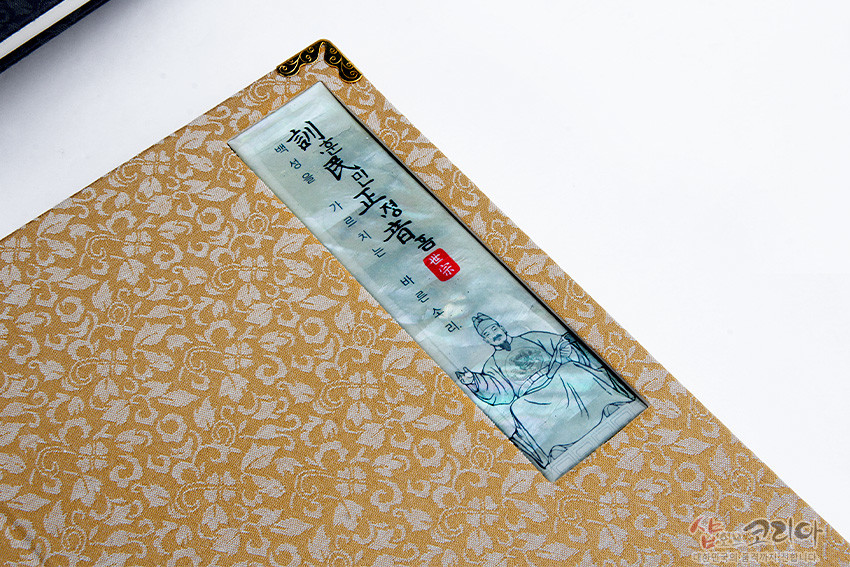 [텍스트: 訓民正音 解例 序文] 황금색 비단 위 은은한 꽃무늬 문양과 세종대왕 초상 자개 인lay, 모서리 금속 장식이 어우러진 전통 노트 표지 이미지