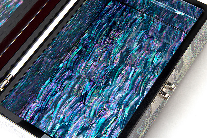 [텍스트: ] 다채로운 청록·보라빛 자개를 촘촘히 상감한 내부 장식, 옻칠 마감으로 유광을 더한 나전칠기 굴림무늬 보석함 내부 표현