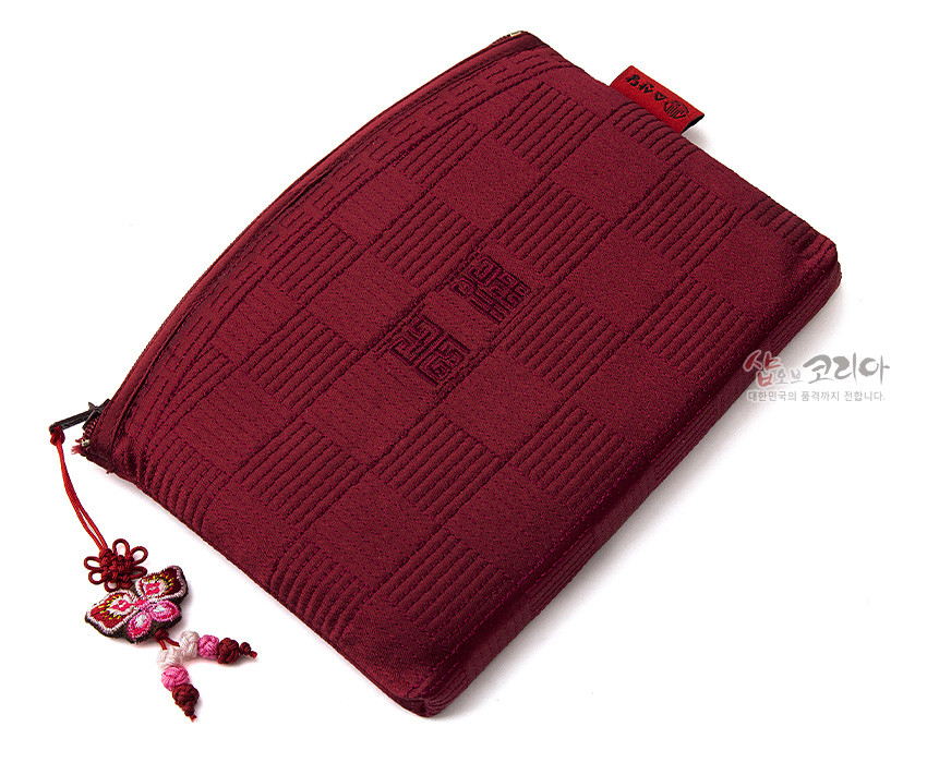 [텍스트: 샵오브코리아 대한민국의 품격까지 전합니다.] 적갈색 비단 누비 원단 위 격자 직조와 중앙 전통 문자 문양, 나비 모양 매듭 장식이 달린 지퍼형 파우치 디자인
