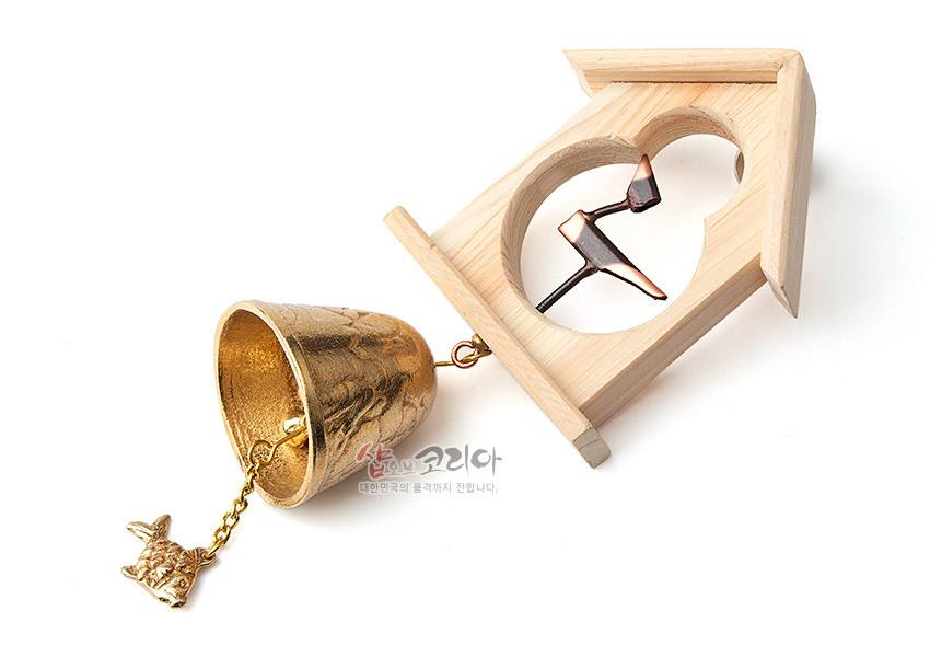 [텍스트: 샵오브코리아 대한민국의 혼까지 전달합니다.] 연한 원목 집 모양 틀에 구리빛 솟대 장식과 파도 문양 황동 종, 물고기 모양 금속 추로 구성된 전통 문종 장식