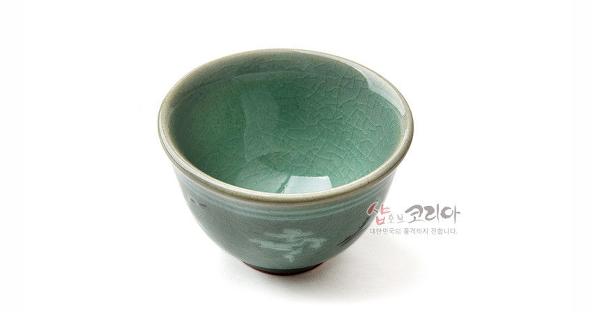 [텍스트: 샵오브코리아 대한민국의 품격까지 전합니다.] 청록색 청자 유약과 자연스러운 균열무늬, 은은한 운학 상감 문양이 조화된 전통 도자기 다완 모습