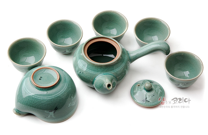 [텍스트: 샵오브코리아 대한민국의 품격까지 전합니다.] 청자 유약과 상감 운학 문양이 조화를 이룬 청록색 도자기 다관과 5인 다완, 균열무늬가 특징인 전통 다기세트 구성