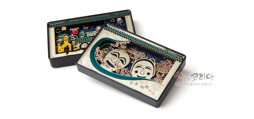 [텍스트: 안동 하회마을, 샵오브코리아 대한민국의 품격까지 전합니다.] 금속 재질 직사각형 마그넷에 하회탈 입체 부조와 하회마을 전경, 분홍 꽃문양과 청록 곡선 장식이 어우러진 디자인