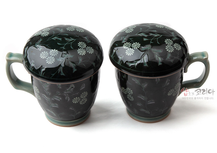 [텍스트: 샵오브코리아 대한민국의 품격까지 전합니다.] 짙은 녹색 유약 위 백색 국화와 넝쿨 상감 문양이 둘러진 뚜껑 포함 흑진사 도자기 머그다기잔 세트 모습