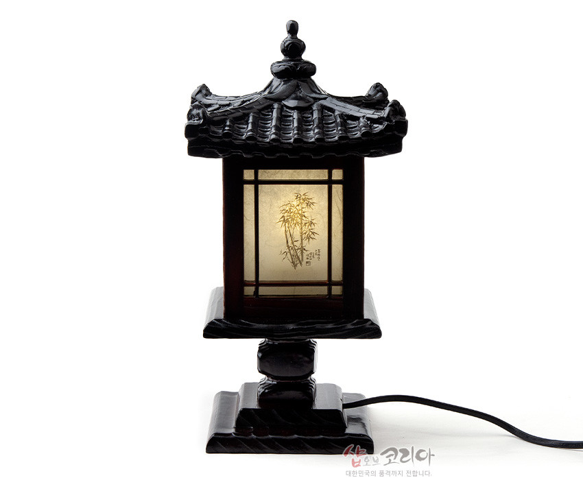[텍스트: 샵오브코리아 대한민국의 품격까지 전합니다] 짙은 흑색 목재로 조각된 기와 지붕과 받침, 반투명 한지 패널에 대나무 문양과 한글 글씨가 비쳐 보이는 전통 미니 좌등 모습