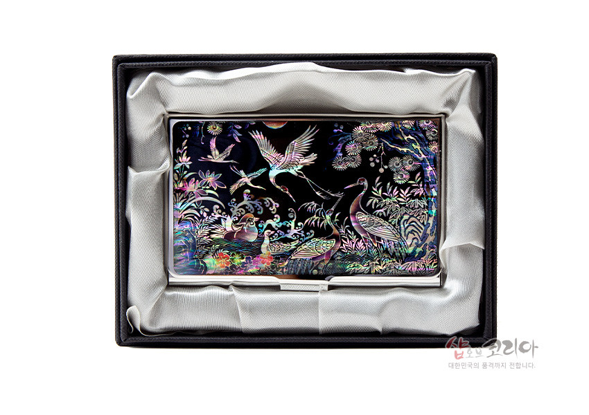 [텍스트: 샵오브코리아 대한민국의 품격까지 전해니다] 흑색 금속 바탕 위 자개 상감 기법으로 송학, 연꽃, 파도와 수풀을 다채로운 오색으로 표현한 명함집 구성