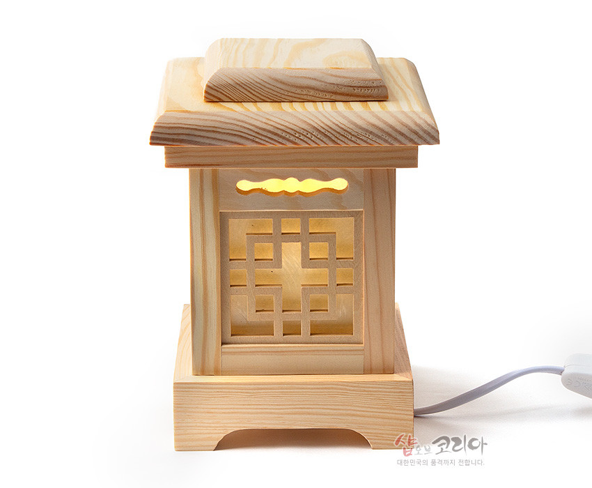 [텍스트: 샵오브코리아 대한민국의 품격까지 전합니다.] 연한 자연색 원목으로 제작된 사각 좌등, 상단 굴곡 지붕과 중앙 완자문살 창살, 내부의 은은한 노란 조명이 비치는 전통 조명 소품
