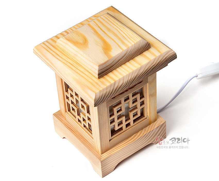 [텍스트: 샵오브코리아 대한민국의 품격까지 전합니다.] 연한 자연색 원목으로 제작된 사각 좌등, 상단 두툼한 목재 지붕 구조와 측면 완자문살 창살로 구성된 전통 목공예 조명 소품