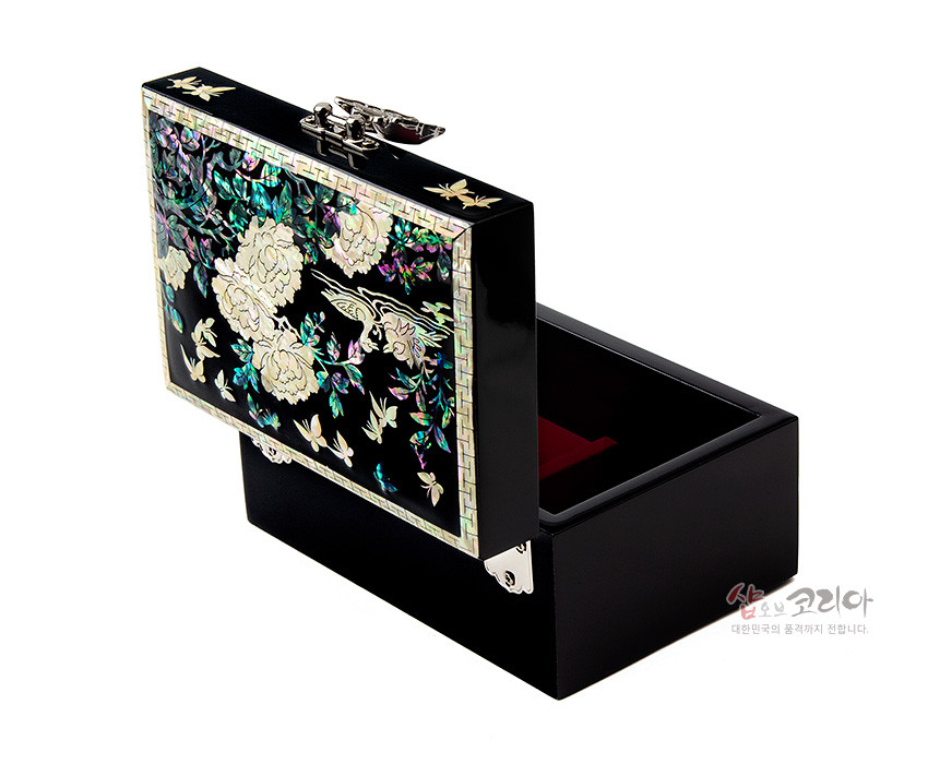 [텍스트: 샵오브코리아 대한민국의 품격까지 전합니다.] 흑색 옻칠 바탕 위 자개 상감 기법으로 모란과 나비, 봉황 문양을 수놓고 은빛 금속 잠금장식과 모서리 장식을 더한 직사각 보석함 이미지 설명
