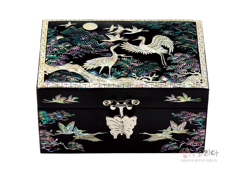 [텍스트: 샵오브코리아 대한민국의 품격까지 전합니다.] 흑색 옻칠 바탕에 자개 상감 기법으로 송학과 소나무, 만월 문양을 수놓고 나비 모양 금속 잠금장식을 더한 직사각 보석함 디자인
