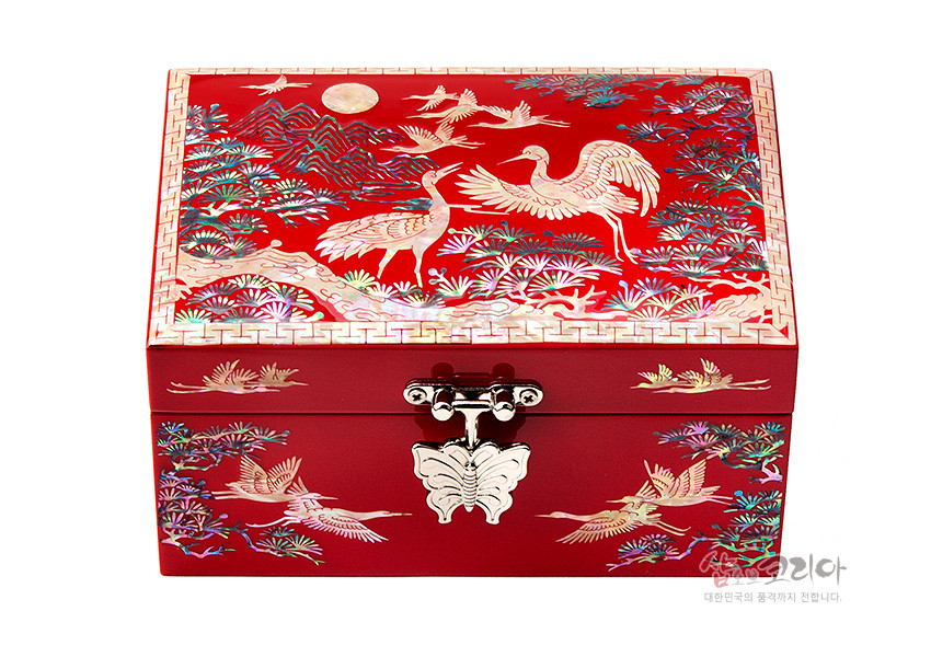 [텍스트: 샵오브코리아 대한민국의 품격까지 전합니다.] 적색 옻칠 바탕 위 자개 상감으로 송학과 소나무, 만월과 산수 문양을 섬세하게 표현한 직사각 보석함 디자인