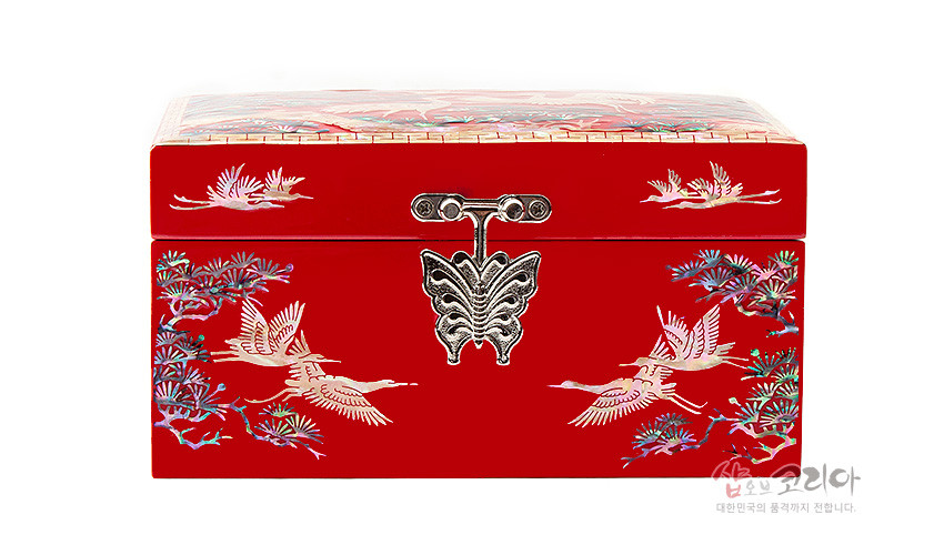 [텍스트: 샵오브코리아 대한민국의 품격까지 전합니다.] 붉은 옻칠 바탕 위 자개 상감으로 소나무와 비상하는 송학 문양을 표현하고 나비 형 금속 잠금장치를 더한 직사각 보석함 정면 디자인
