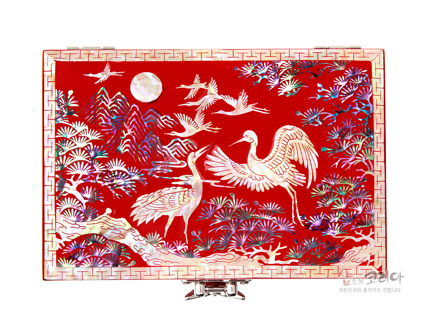 [텍스트: 샵오브코리아 대한민국의 품격까지 전합니다.] 적색 옻칠 바탕 위 자개 상감으로 송학과 소나무, 산수와 만월 문양을 섬세하게 표현한 직사각 보석함 장식