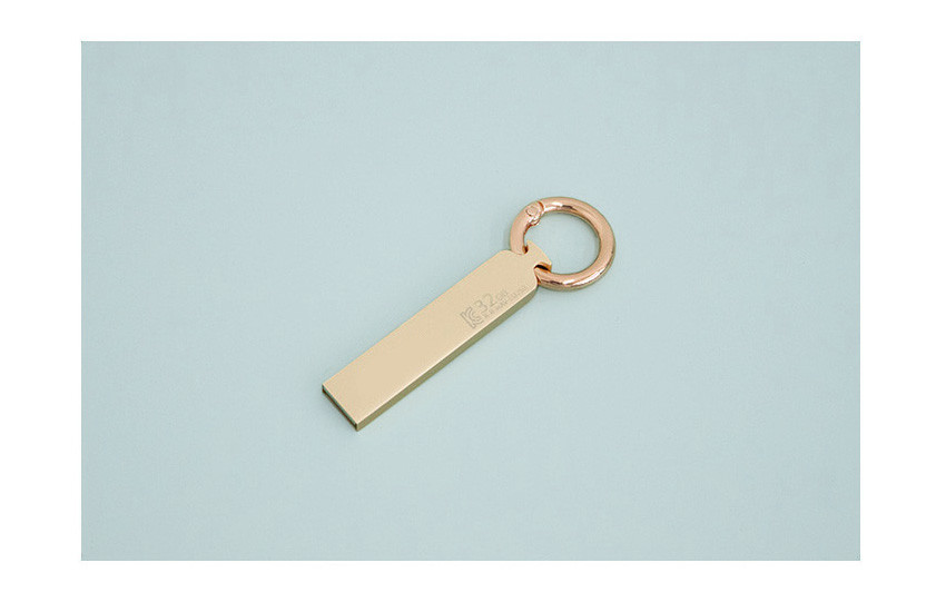 [텍스트: K 32...] 연한 골드 톤의 직사각형 금속 바디와 로즈골드 색 라운드 링이 조화된 USB 일체형 열쇠고리 디자인