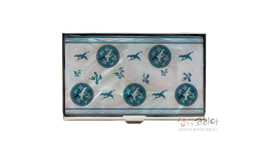 [텍스트: 샵오브코리아 대한민국의 품격까지 전합니다.] 자개 바탕 금속 명함케이스 위 청자색 상감 운학문 원형 문양과 비상하는 학, 테두리 기하학 무늬 장식 이미지 설명