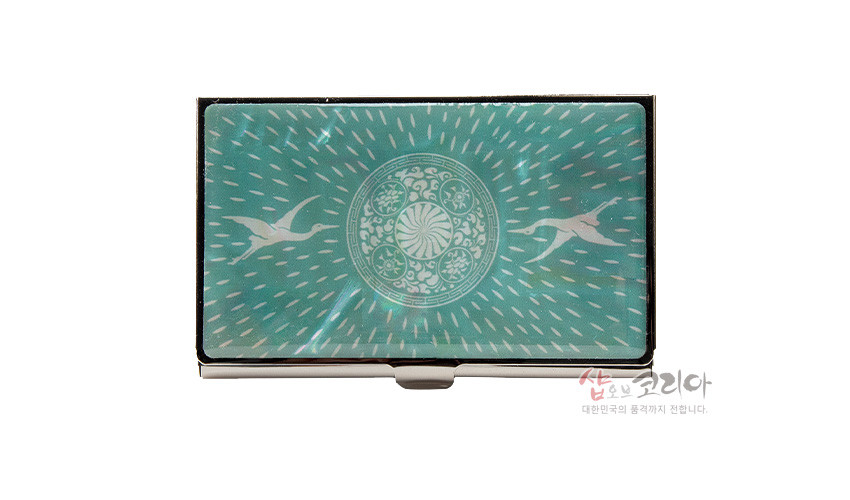 [텍스트: 샵오브코리아 대한민국의 품격까지 전합니다.] 청자색 금속 명함케이스, 자개 상감 기법의 원형 연꽃문과 비상하는 백학 문양, 방사형 빛줄기 장식 디자인