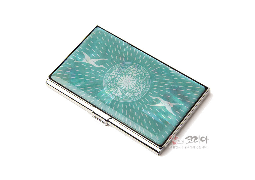 [텍스트: 샵오브코리아 대한민국의 좋은제품이 전합니다.] 청자색 금속 명함케이스 위 자개 상감 기법, 방사형 빛 무늬와 원형 연꽃·학 문양 장식 디자인