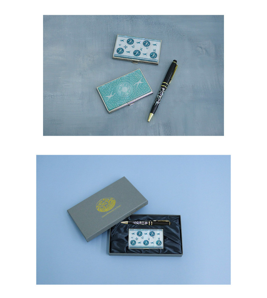 [텍스트: KOREAN HERITAGE] 금속 재질 위 청자색 운학문 상감과 기하학 원형 문양이 있는 명함케이스, 흑색 바탕에 은색 운학문이 새겨진 금속 볼펜과 전통문양 금박 로고 인쇄 패키지 박스 구성 이미지