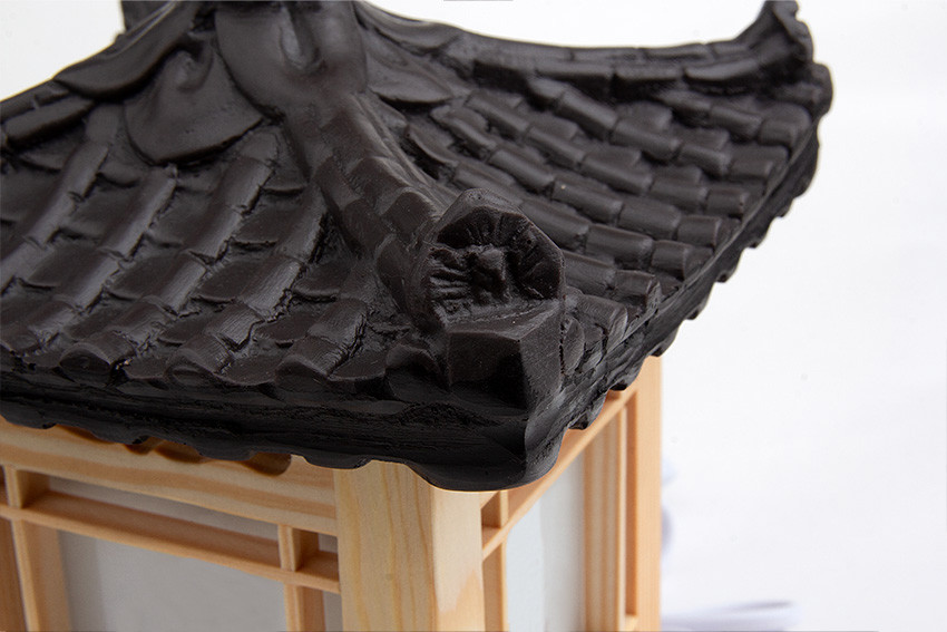 검은 기와지붕을 사실적으로 형상화한 상부와 밝은 원목 창살 구조, 반투명 백색 창호지가 조화를 이루는 전통 한옥 미니어처 조명등 디테일 이미지