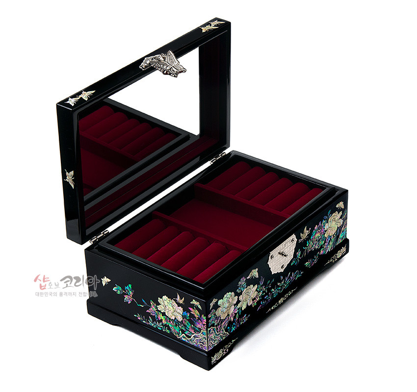 [텍스트: 샵오브코리아 대한민국의 품격까지 전하는] 흑색 옻칠 바탕 위 자개 상감 목단과 나비 문양, 은은한 오색광과 금속 잠금장치, 붉은 벨벳 내부 칸막이로 구성된 직사각 보석함 이미지 설명