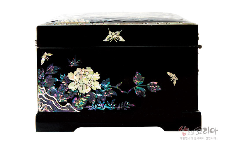 [텍스트: 샵오브코리아 대한민국의 품격까지 전합니다.] 흑색 옻칠 바탕에 자개 상감으로 표현한 목단꽃과 나비, 나뭇가지 문양의 직사각형 보석함 측면 장식 모습