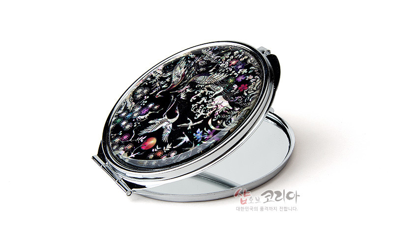 [텍스트: 샾오브코리아 대한민국의 품격까지 전합니다.] 흑색 옻칠 바탕에 자개 상감 기법으로 소나무와 학, 파도와 꽃 문양을 섬세하게 표현한 타원형 금속 손거울 디자인