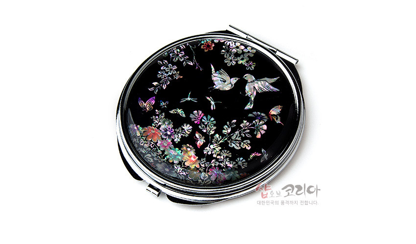 [텍스트: 샵오브코리아 대한민국의 품격까지 전합니다.] 흑색 옻칠 바탕 위 자개 상감 기법으로 새와 꽃, 나비와 잠자리를 섬세하게 표현한 원형 금속 손거울 디자인