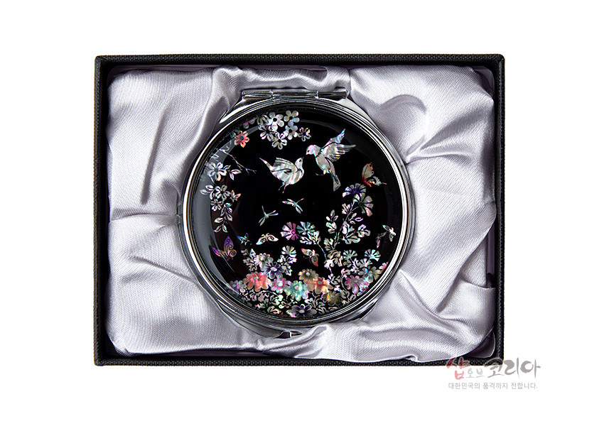 [텍스트: 샵오브코리아 대한민국의 품격까지 전합니다.] 흑색 옻칠 바탕 위에 천연 자개 상감 기법으로 꽃과 새, 나비와 잠자리 등을 섬세하게 표현한 원형 금속 손거울 모습