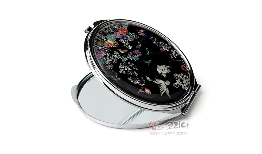 [텍스트: 샵오브코리아 대한민국의 품격까지 전달합니다.] 흑색 옻칠 바탕 위 자개 상감 기법으로 꽃과 새, 나비 문양을 섬세하게 표현한 타원형 금속 손거울 디자인