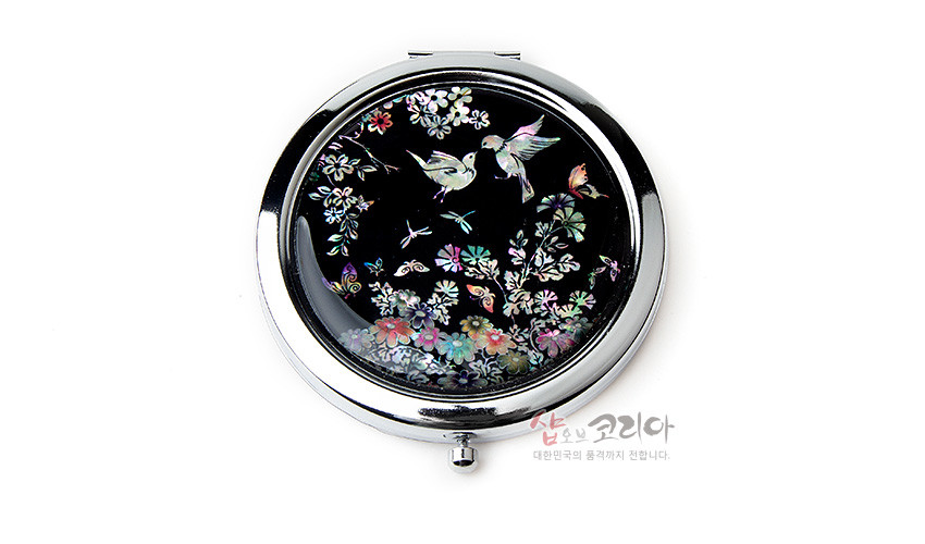 [텍스트: 샵오브코리아 대한민국의 품격까지 전합니다.] 흑색 바탕 위 천연 자개 상감 기법으로 화조도와 꽃, 나비, 잠자리 문양을 표현한 원형 금속 손거울 디자인