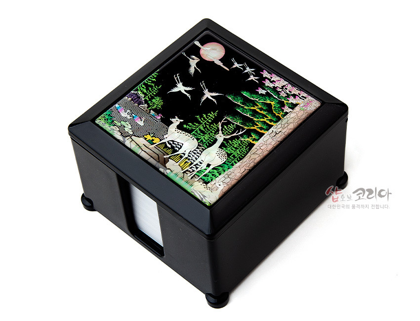 [텍스트: 샵오브코리아 대한민국의 품격까지 전합니다.] 흑색 옻칠 사각 상자 위 자개 상감 기법으로 사슴·학·소나무·해를 표현한 십장생 민화 문양 메모지함 이미지 설명