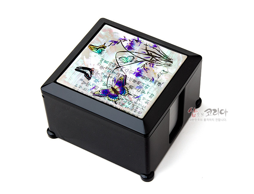 [텍스트: 샵오브코리아 대한민국의 품격까지 전합니다.] 흑색 옻칠 사각 메모지함 상판에 자개 상감 기법으로 표현된 난초와 나비, 한글 문양이 어우러진 디자인