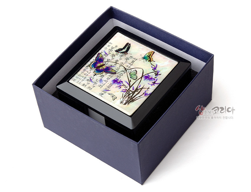 [텍스트: 샵오브코리아 대한민국의 혼을까지 전합니다.] 흑색 옻칠 메모지함 상판에 자개 상감 난초와 나비, 한글 문양이 어우러진 사각 형태 디자인