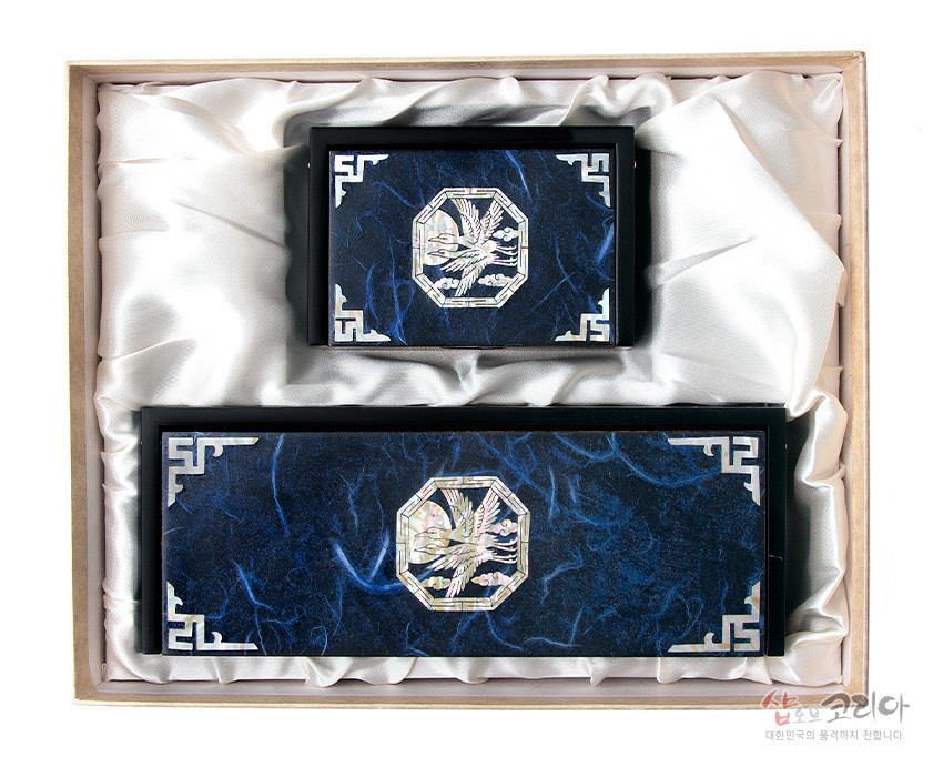 [텍스트: 샵오브코리아 대한민국의 품격까지 전합니다.] 짙은 청색 한지 바탕 위 자개 상감 청학 문양과 백색 기하학 모서리 장식이 어우러진 필함·명함함 세트 이미지