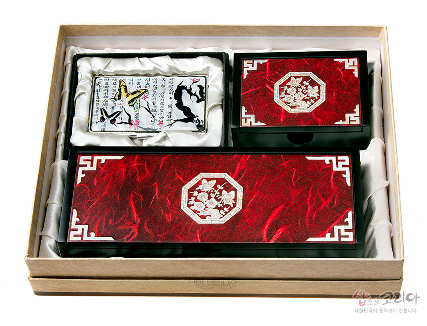 [텍스트: 샵오브코리아 대한민국의 품격까지 전합니다] 붉은 한지 질감 바탕에 백색 매화와 전통 문양을 자개로 상감한 필함·명함함·명함케이스 세트 구성