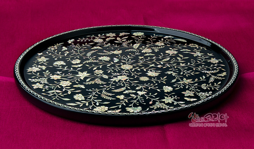 [텍스트: 샵오브코리아 대한민국의 전통거치 문화를 전합니다.] 짙은 흑색 옻칠 바탕 위 자개 상감으로 표현된 섬세한 넝쿨과 꽃문양, 가장자리에 연속문으로 장식된 원형 나전칠기 쟁반 이미지 설명